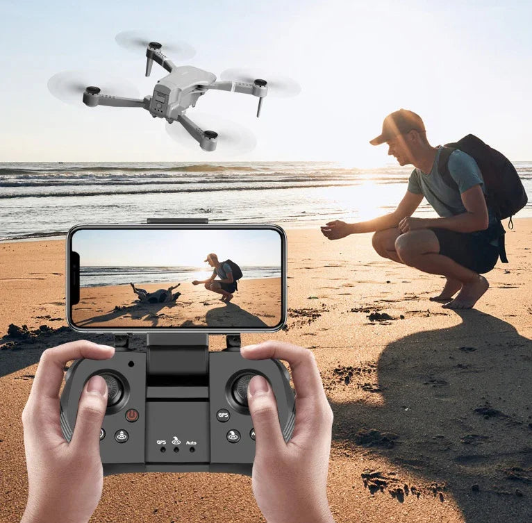 Hombre controlando dron con cámara 4K en la playa al atardecer, usando control remoto y smartphone
